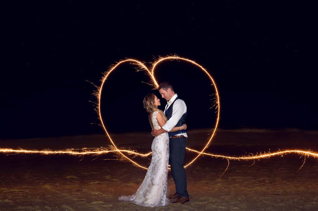 bride and groom on beach with long exposure heart sparkler around them
