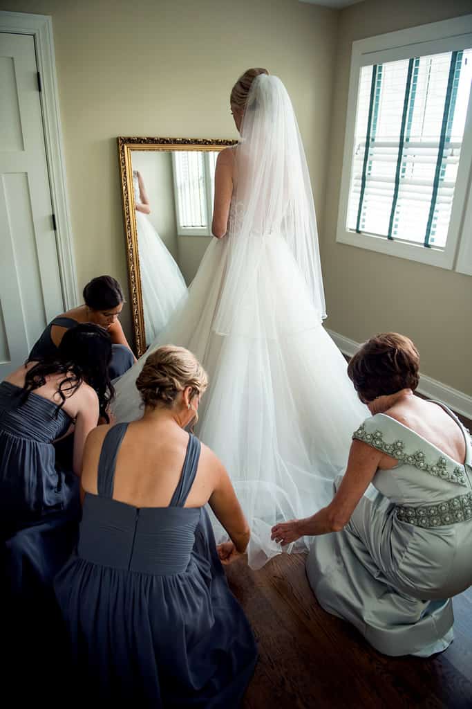 bridesmaids fixing bride's train while getting ready